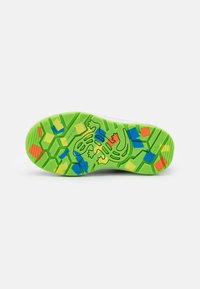 Semelle de chaussure en caoutchouc vert avec un motif hexagonal, ornée d'accents géométriques colorés en bleu, orange et jaune, ainsi qu'un design de grenouille.