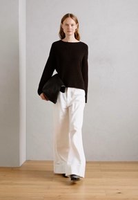 Maglione nero a coste, pantaloni bianchi a gamba larga, in mano una pochette nera. Design semplice, texture liscia, colori neutri, accenti minimali.