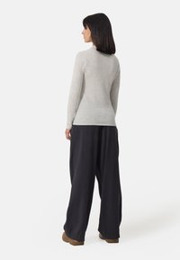 Szary, dopasowany sweter z długimi rękawami, w połączeniu z luźnymi, czarnymi, plisowanymi spodniami i brązowymi płaskimi butami. Miękka faktura i prosty design.