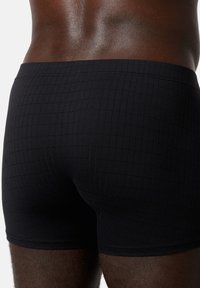 Sorte boxershorts med en tekstureret gittermønster, lavet af et glat materiale, med en tætsiddende pasform og elastisk talje.