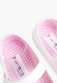 Zapatillas de lona blancas con un forro de cuadros rosa. Incluyen una etiqueta con "Pisamonas" impresa en letras de colores. Diseño clásico sin cordones.