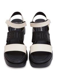 Sandales ouvertes noires et beiges avec semelles épaisses, brides beiges réglables sur les orteils et les chevilles, et bandes élastiques noires avec le texte "FASHION".