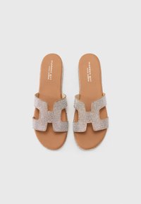 Lys brun slide-sandaler med metallisk teksturerte stropper som har et geometrisk utskjæringsdesign, og en glatt beige innersåle.