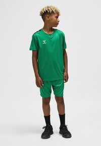 Grön sportig fotbollsuniform av lättviktsmaterial; inkluderar en kortärmad tröja och shorts med svarta detaljer på axlarna.