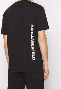 Černé tričko vyrobené z bavlny s krátkými rukávy, na zádech s vertikálním bílým logem "KARL LAGERFELD". Jednoduchý design.