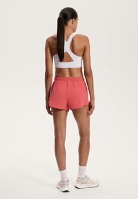 White sports bra with a cutout back; pink athletic shorts with an elastic waistband; white socks; light sneakers.
