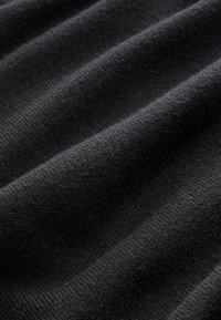 Fekete kötött szövet, puha tapintású, bordázott felülettel és finom mintával, amelyet a váltakozó redők hoznak létre.