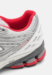 Buty sportowe z białą, przewiewną siateczką, czerwonymi akcentami i szarym podniszczem z widocznymi poduszkami amortyzacyjnymi. Numer modelu: 1906R.