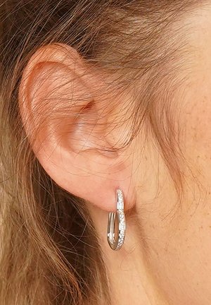 Silberne Ohrhänger mit einem verdrehten Design, das eine strukturierte Oberfläche und kleine klare Akzente aufweist, getragen am Ohrläppchen einer Person.