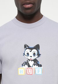 Light purple cotton t-shirt featuring a cartoon cat with a black and white color scheme, accompanied by colorful block letters spelling "HUF."