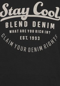 Felpa nera con cappuccio e testo bianco: "Rimani Fresco", "Blend Denim" e "Rivendica i Tuoi Diritti sui Jeans", con una disposizione rotonda e stabilita nel 1993.
