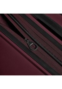 Bordeaux kleurige stoffen koffer met een gestructureerd oppervlak, twee zwarte ritsen en een glanzend zwarte handgreep als accent. Zichtbare stiksel detail.