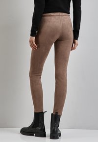 Leggings in suede marrone con un design aderente, texture liscia e vita alta, abbinati a stivaletti neri con lati elasticizzati.