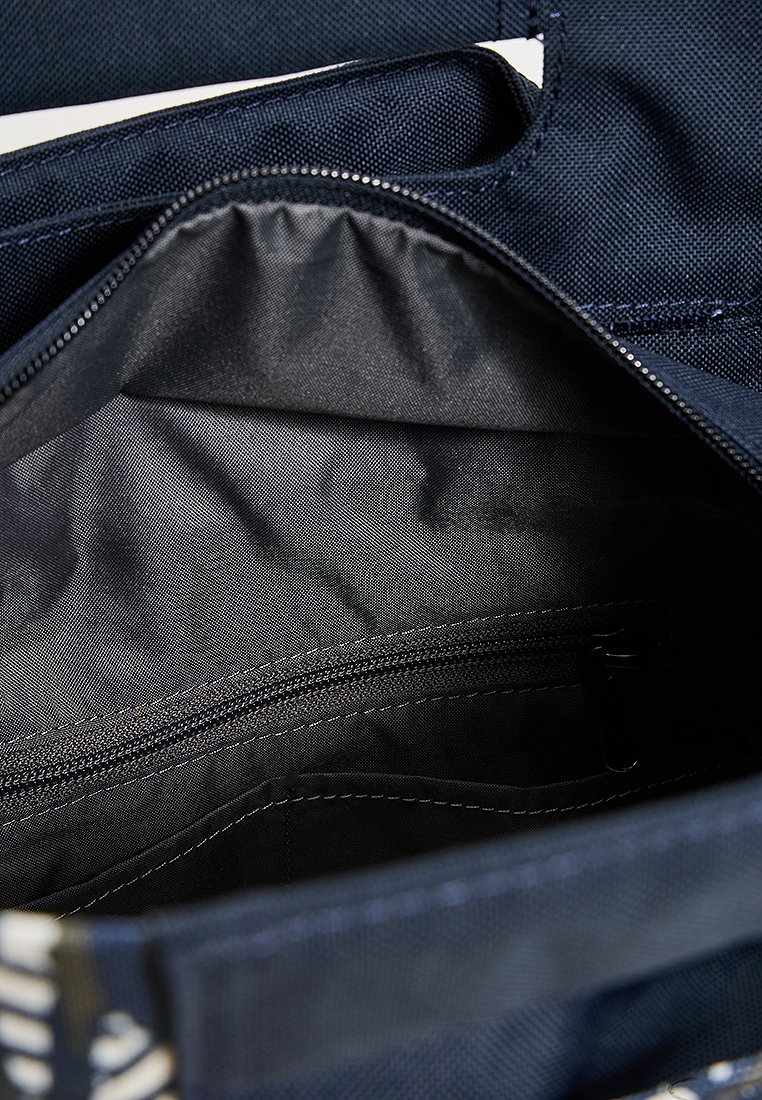 Innenseite einer marineblauen Stofftasche mit glatter Textur, ausgestattet mit einer Reißverschlusstasche und einfarbigem dunklen Futter. Oben sind doppelte Griffe sichtbar.