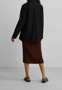 Schwarzer taillierter Blazer, gerippter brauner Midirock und haustierähnliche Slipper. Glatter Stoff mit strukturierter Passform und texturiertem Design.