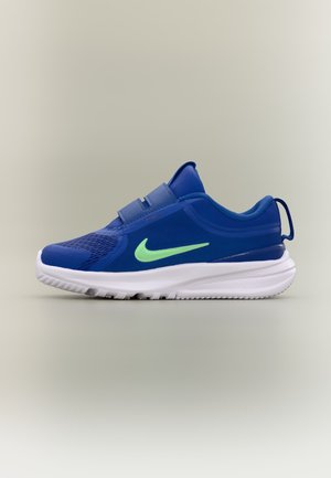 Chaussure de sport bleue avec deux bandes velcro, logo Nike vert clair sur le côté, semelle blanche et languette au talon sur fond uni.
