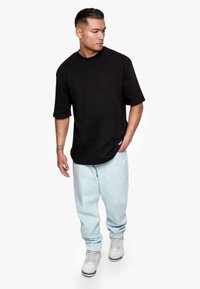 Black short-sleeve t-shirt with a round neck, paired with light blue baggy jeans and white sneakers with gray and yellow accents.