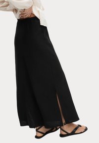 Svart maxikjol i lätt tyg med en sidoöppning och elastisk midja, kombinerad med platta svarta sandaler med korsade remmar.