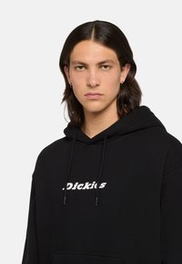 Sudadera con capucha negra hecha de tela suave, con un logotipo blanco impreso en la parte delantera, cuerdas ajustables y un bolsillo frontal.