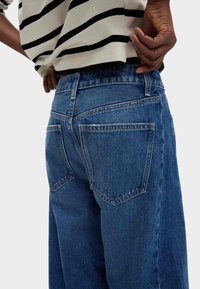 Blauwe denim spijkerbroek met een hoge taille, voorzien van twee achterzakken, zichtbare stiksels en een gestructureerde stof. De tailleband heeft een lichte stretch.