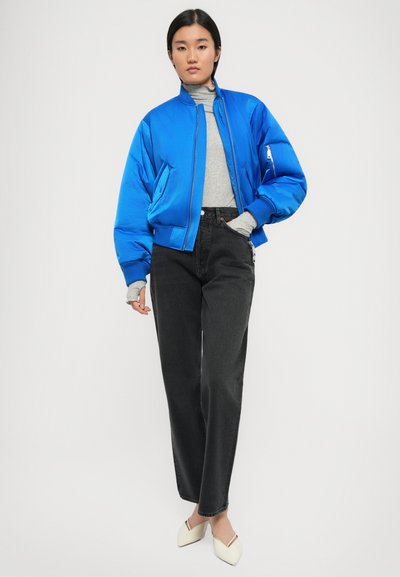 Blaues Bomberjackett mit Reißverschluss, kombiniert mit einem grauen Rollkragenpullover, schwarzen Jeans und cremefarbenen Ballerinas. Verfügt über weite Ärmel und Seitentaschen.