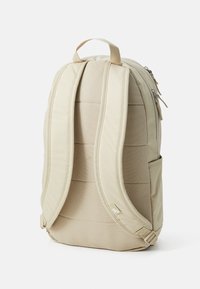 Beige rugzak met gewatteerde schouderbanden, textiele stof, zijvak en dubbele ritsen. Voorzien van een versterkte handgreep aan de bovenkant voor gemakkelijk dragen.