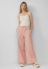 Pantalon léger rayé en corail et blanc, avec une taille élastique et des poches latérales. Associé à un débardeur beige et des sandales à plate-forme.