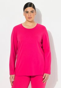 Langärmliges Oberteil aus lebhaftem pinkfarbenen Stoff mit einem runden Ausschnitt. Glatte Textur, oversized Schnitt, kombiniert mit passenden pinkfarbenen Hosen.