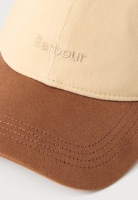 Μπεζ και καφέ καπέλο μπέιζμπολ με κεντημένο το λογότυπο "Barbour" στην μπροστινή πλευρά και ορατή ραφή στο γείσο.