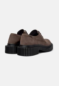 Zapatos de piel marrón con suelas negras acanaladas, mostrando los ángulos trasero y lateral, resaltando los detalles de los cordones y la textura.