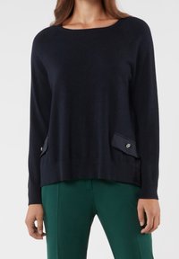 Pull en maille bleu marine avec un col rond, des manches raglan et deux poches latérales ornées de boutons décoratifs. Texture douce.