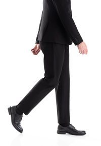 Suit nero su misura con pantaloni slim-fit, scarpe eleganti in pelle nera lucida con dettagli brogue e finitura liscia.