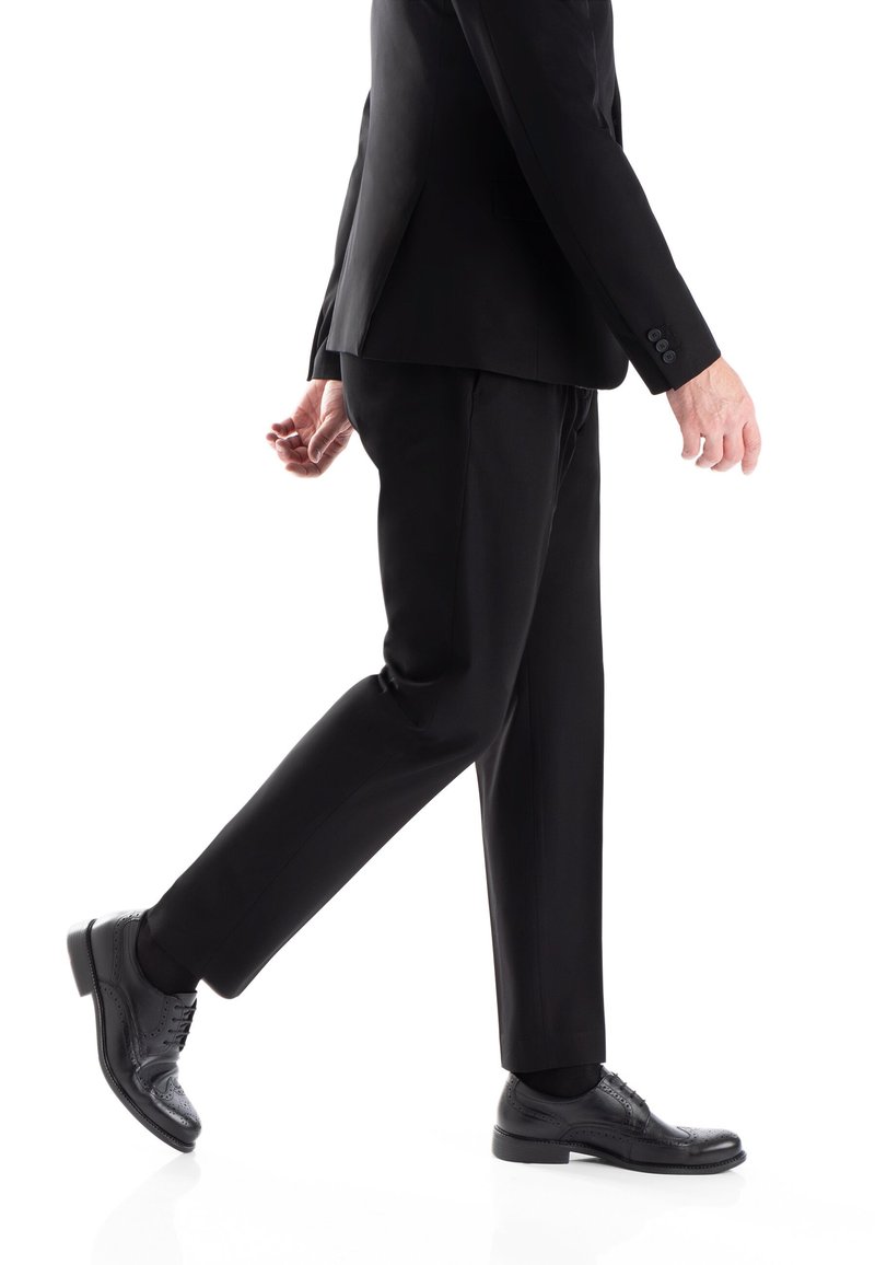 Suit nero su misura con pantaloni slim-fit, scarpe eleganti in pelle nera lucida con dettagli brogue e finitura liscia.