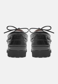 Schwarze Lacklederbootsschuhe mit niedrigem Profil, abgerundeter Zehenpartie und Gummisohle. Mit einem Schnürdesign, das zwei Ösen und Nähdetails aufweist.