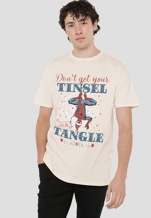 Junger Mann in einem beigen T-Shirt mit einem umgedrehten Spider-Man und dem Text "Lass deine Girlanden nicht durcheinander geraten" in Rot und Blau.