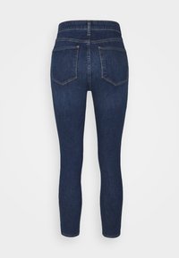 Mörkblå denimjeans sedda bakifrån. Har hög midja, två bakfickor och smal benslut med minimala sömdetaljer.