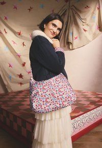 Borsa a tracolla con motivo floreale in tessuto di cotone blu e rosso, con una tracolla spessa e morbida. Presenta una forma spaziosa e arrotondata e una texture soffice.