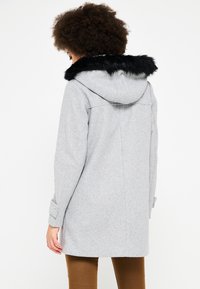 Šedý kabát s černou umělou kožešinou na kapuci, dlouhými rukávy a detaily na manžetách se zacvakávacími knoflíky. Má čistý, rovný design zadní části.