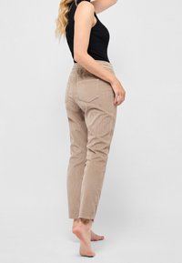 Beige kordflorsbyxor med en figursydd design, med två bakfickor och en texturerad yta. Bärs med en svart ärmlös topp.