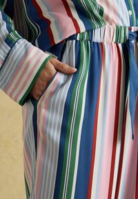 Multicolored striped shirt with blue, green, pink, and red tones; made of smooth fabric; features a pocket and elastic waistband.