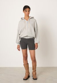 Siva jopa z zadrgo in vrvicami, kombinirana s temno sivimi kratkimi hlačami in rjavimi škornji do kolen. Tkanina je videti mehka in zračne oblike.