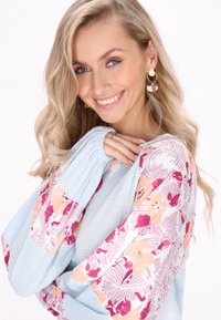 Top azzurro chiaro con maniche a fantasia floreale nei toni del rosa e pesca. Presenta polsini arricciati e un design dalla vestibilità rilassata.