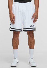 White basketball shorts with black side stripes and logo, made of mesh fabric. Elastic waistband, mid-thigh length, paired with white socks and shoes.