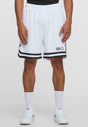 Shorts de basketball blancs avec des bandes latérales noires et un logo, en tissu en maille. Taille élastique, longueur mi-cuisse, assortis de chaussettes et de chaussures blanches.