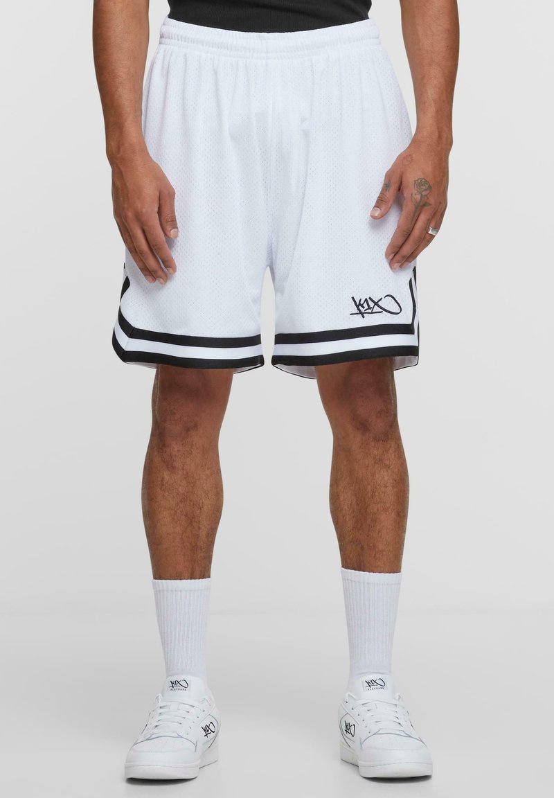 White basketball shorts with black side stripes and logo, made of mesh fabric. Elastic waistband, mid-thigh length, paired with white socks and shoes.