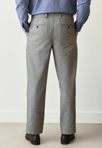 Graue, gewebte Hose mit geradem Bein, ausgestattet mit zwei Gesäßtaschen mit Knöpfen und einer glatten Textur. Kombiniert mit braunen Schuhen.