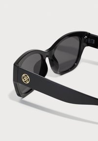 Schwarze Sonnenbrille mit einem eleganten, kantigen Design. Dunkle Gläser und glatte Kunststoffrahmen. Der Bügel verfügt über ein goldfarbenes Logodetail.