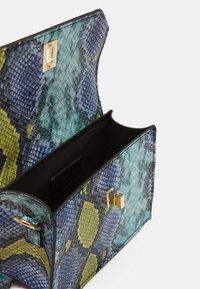 Sac à main imprimé serpent aux nuances bleues et vertes, présentant une forme structurée, une surface texturée et une fermeture en métal doré. Intérieur ouvert visible.