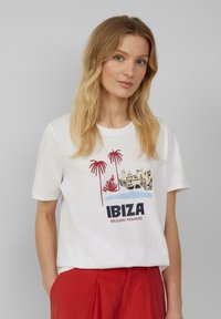 T-shirt en coton blanc avec un imprimé coloré de palmiers et le texte "IBIZA BALEARIC PARADISE", à manches courtes et coupe décontractée.