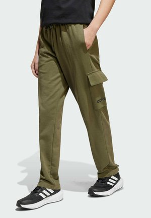 Pantaloni cargo verde oliva con vita regolabile tramite cordino, tasche laterali e logo Adidas, abbinati a sneakers nere con strisce bianche.